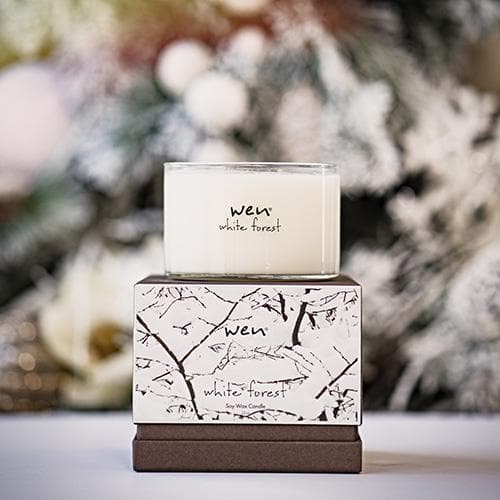 Lifestyle image of the white forest candle against a background of trees